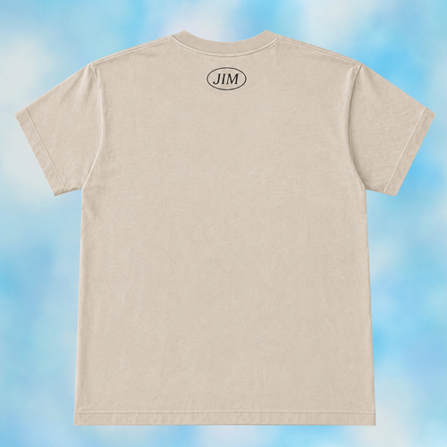 A light beige crewneck t-shirt shown from the back, featuring a small black oval logo with the letters 'JIM' centered near the neckline. The t-shirt is displayed against a soft, cloudy blue and white background.