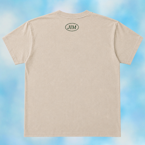 A light beige crewneck t-shirt shown from the back, featuring a small black oval logo with the letters 'JIM' centered on the upper back. The t-shirt is displayed against a soft, cloudy blue and white background.